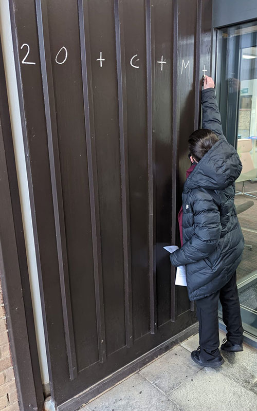 Student writing in chalk on the door for The Feast of the Epiphany